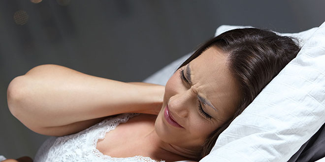 девушка мучается с болью в шее лежа в кровати