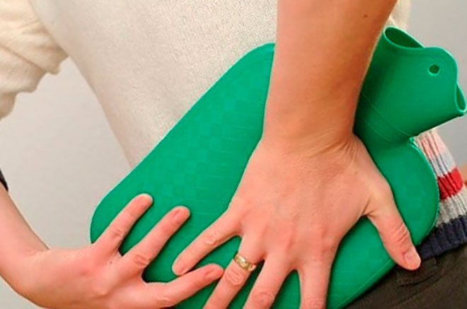 женщина с остеохондрозом держит грелку на пояснице